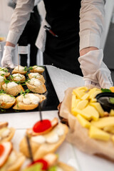 Close-up view of a catering table with an assortment of canapés and cheese slices, served by individuals in white gloves