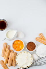 Ingredients for preparing the Italian dessert tiramisu. Savoiardi cookies, mascarpone, yolks, coffee, cream and cocoa on a light background, top view.