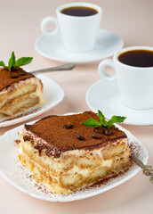 Two pieces of tiramisu with mint and a cup of coffee. Classic Italian dessert..
