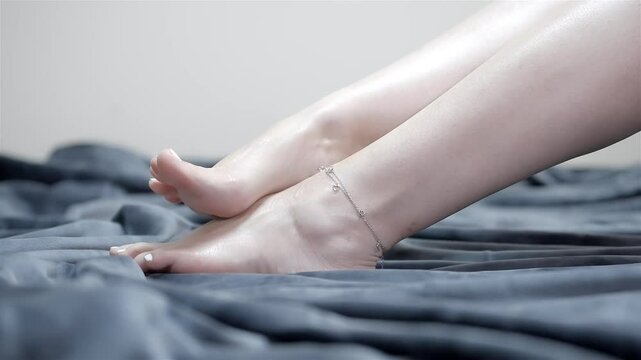 Woman arches foot as she strokes opposite leg back and forth rubbing on top of blanket