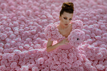 Beautiful woman in the dress of roses  in the garden with giant roses