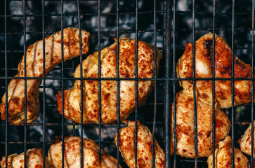 Evenly laid out on barbecue grill, chicken pieces are fried on the fire, gaining juiciness and a crispy crust.