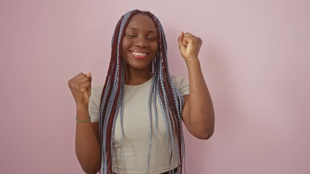 Joyful african american woman ecstatically screams her win, standing victoriously against a quirky pink isolated background