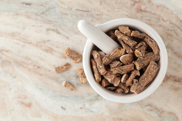 Top-view of Dry Organic Sweet flag or Vach (Acorus calamus) roots, in white ceramic mortar and pestle, on a marble background.