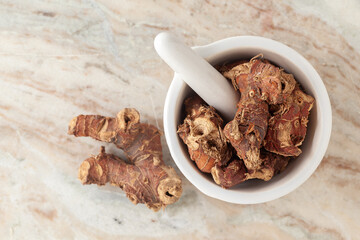 Top-view of Dry Organic Kulanjan (Alpinia galanga) roots, in white ceramic mortar and pestle, on a...