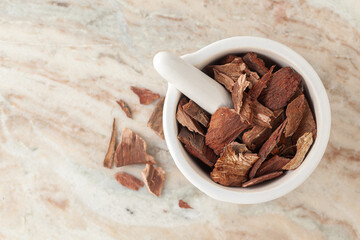 Top-view of Dry Organic Arjuna (Terminalia Arjuna) Barks, in white ceramic mortar and pestle, on a marble background.