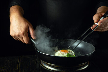 Cooking scrambled eggs in a frying pan. The chef holds a fork and a frying pan with a fried egg. Low key concept of preparing breakfast