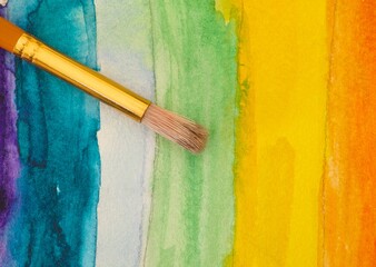A close-up shot of a paintbrush on a rainbow watercolour background.