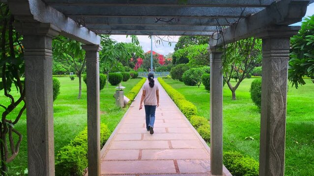 Young Indian woman walks along the path in the cubbon park in a white shirt and jeans in Bangalore, india
