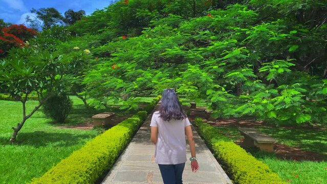 Young Indian woman walks along the path in the cubbon park in a white shirt and jeans in Bangalore, india
