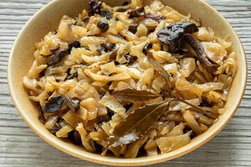 Sauerkraut with dried wild mushroom and laurel leaves, decorated with halved mushroom and laurel sprig. Rustic wooden table.