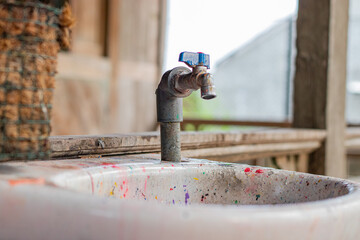 Dirty outdoor faucet sink and sink full of paint, with Asian Indonesian house in the background