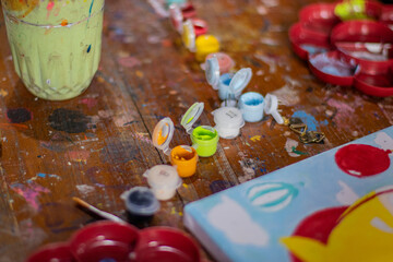 Palette with paints and brushes displayed on a wooden table. a messy table full of watercolor paints