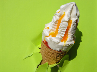 cold delicious ice cream with apricot jam in a waffle cone through a torn hole on a green paper...
