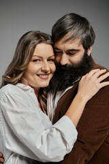 A loving couple poses together, the woman smiling warmly as she rests her head on her bearded partners shoulder.