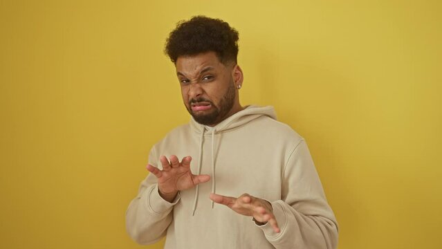 Distraught african american man in hoodie, displaying fear and disgust reaction with hands up, isolated on a yellow background