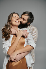 A couple in elegant attire embraces each other in a studio setting.