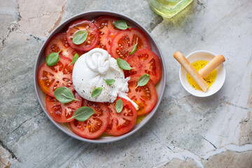 Burrata cheese served with red tomatoes and green basil leaves, above view on a grey granite background, horizontal shot