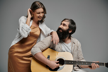 A man plays the guitar while a woman smiles at him.