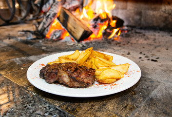 White plate with roast beef and rustic fries. Delicious plate of food in front of the fire.