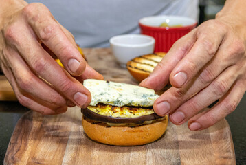 Chef hands starting the preparation of a vegetarian hamburger with bread, eggplant, cheese and sausage. Burger prepared on a restaurant kitchen. Professional chef is preparing burger. Burger making.