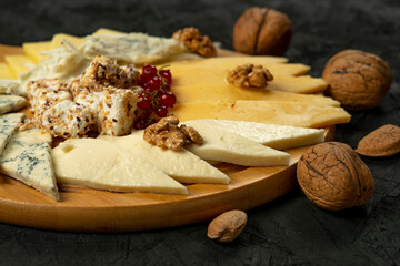 Cheese platter with various types of cheese and nuts on black background