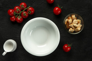 Empty white plate with cherry tomatoes and croutons on black background