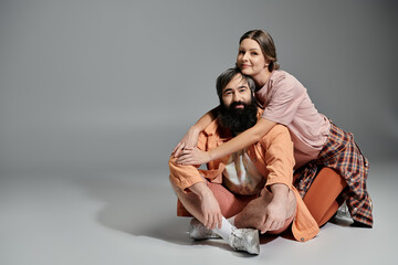 A loving couple, dressed in sophisticated attire, poses together in a studio setting. The woman is embracing the man from behind.