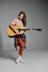 Fototapeta premium A young woman in stylish attire strums an acoustic guitar with passion.