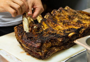 Chef's hands removing a bone from a large piece of meat in restaurant kitchen. Meat being prepared to be served.