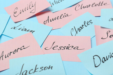Paper stickers with different names on light blue background, closeup. Choosing baby's name
