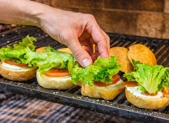 Chef hands starting the preparation of hamburgers in the grill with bread, salad and sausage. Delicious burger prepared on a restaurant kitchen. Professional chef is preparing burger. Burger making.