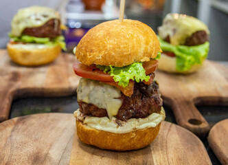 Delicious hamburger with bread, meat, cheese, bacon, salad and sausage on top of wooden board. Professional chef prepared a burger. Burger making.