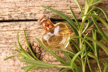 Aromatic essential oil in bottle and rosemary on wooden table, flat lay