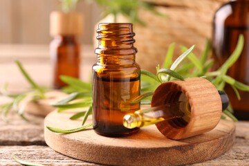 Aromatic essential oil in bottle, pipette and rosemary on wooden table, closeup