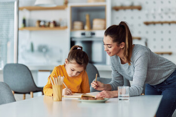 A caring mother and daughter bonding and drawing together at home with colored pencils