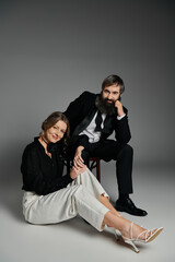 A loving couple dressed in formal attire pose together against a gray backdrop.