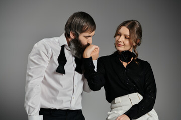A man in a white shirt and bowtie kisses the hand of a woman in a black blouse.