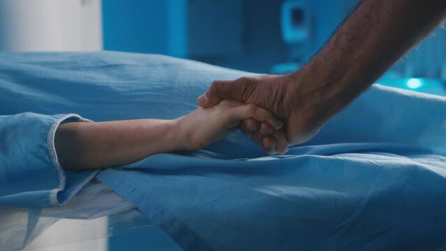 Slowmo close-up of unrecognizable woman holding hand of partner before undergoing medical diagnostic procedure or treatment, lying on patients table in hospital