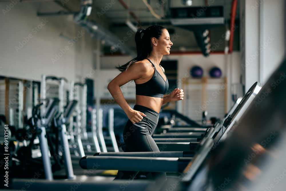 Wall mural side profile of a smiling fit woman running on a treadmill at the gym.