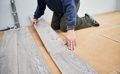 Close up of man construction worker installing laminate timber flooring in apartment under...