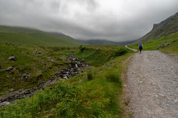 Fototapeta premium Hiker girl on Devils Ladder, one of most difficult trails, that is leading to highest Irish mountain Carrauntoohill or Carrantuohill is the highest mountain in Ireland at 1038m