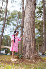 Young girl in pink dress touching tree, exploring national park. Captures wonder and joy of family vacation in nature. Bright sunny day, forest setting, green surroundings.