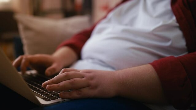 Close-up plump hands of large-bodied man working on laptop, sitting on couch