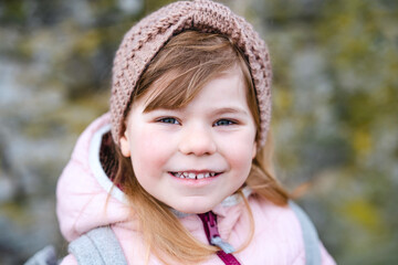 Portrait of happy smiling toddler girl outdoors. Little child with blond hairs looking and smiling at the camera. Happy healthy child enjoy outdoor activity and playing.