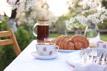Stylish table setting with tea and croissants in spring garden
