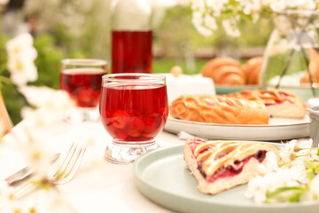 Stylish table setting with beautiful spring flowers, fruit drink and pie in garden