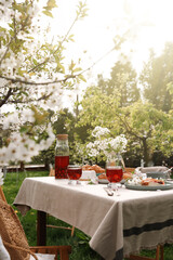 Stylish table setting with beautiful spring flowers, fruit drink and pie in garden