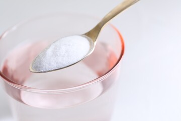 Spoon with baking soda over glass of water on white background, closeup. Space for text