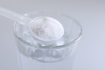 Spoon with baking soda over glass of water on light grey background, closeup